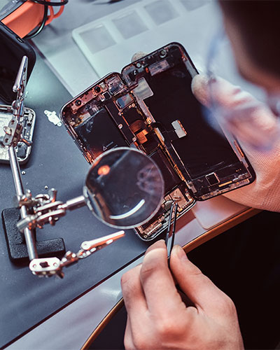 Técnico de reparación usa lupa y pinzas para reparar un teléfono inteligente dañado (foto de primer plano de un teléfono inteligente desmontado).